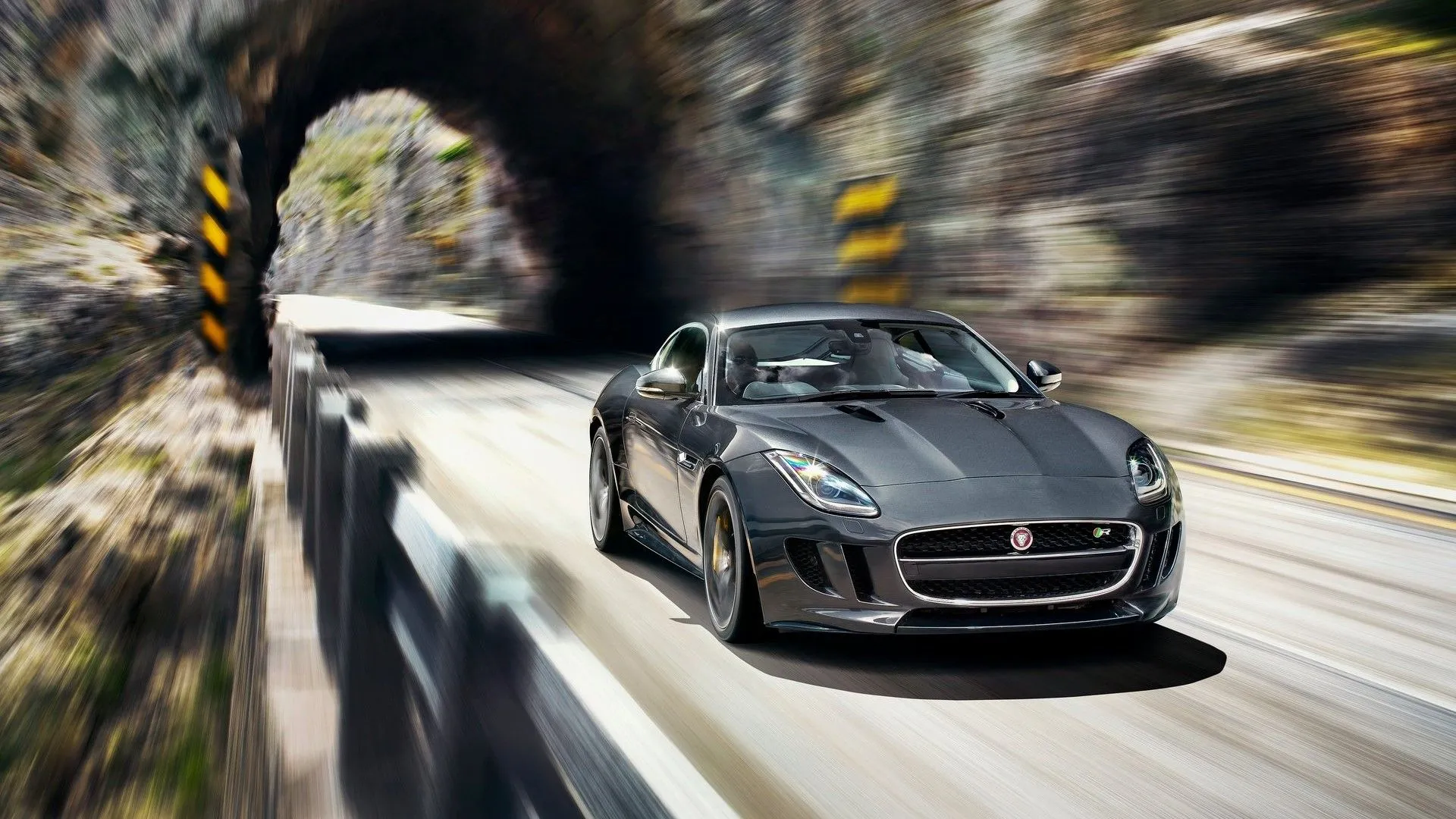 Jaguar F-Type R 2015 màu xanh lam đang tăng tốc ra khỏi đường hầm, góc nhìn 3/4 từ phía trước, thể hiện sự mạnh mẽ và sang trọng