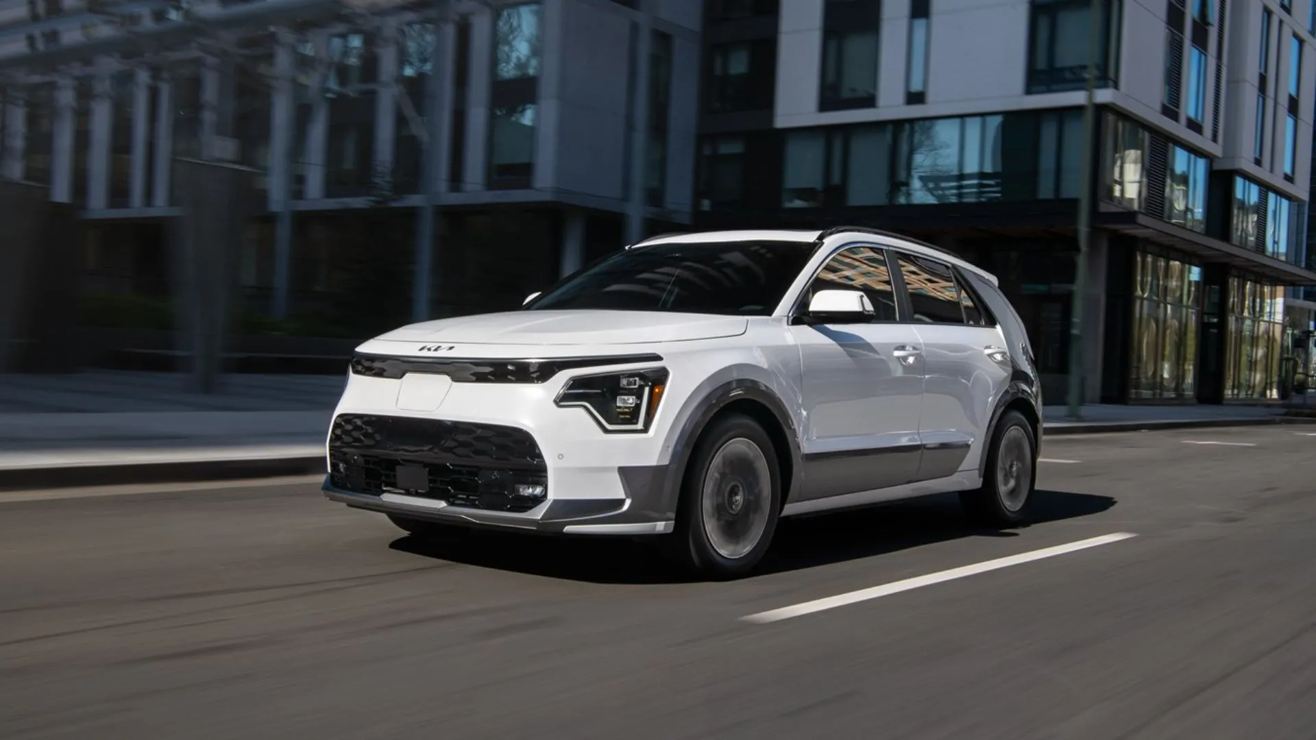 Kia Niro EV 2025 màu trắng di chuyển trên đường phố, mẫu xe điện đô thị tiện lợi và tiết kiệm.