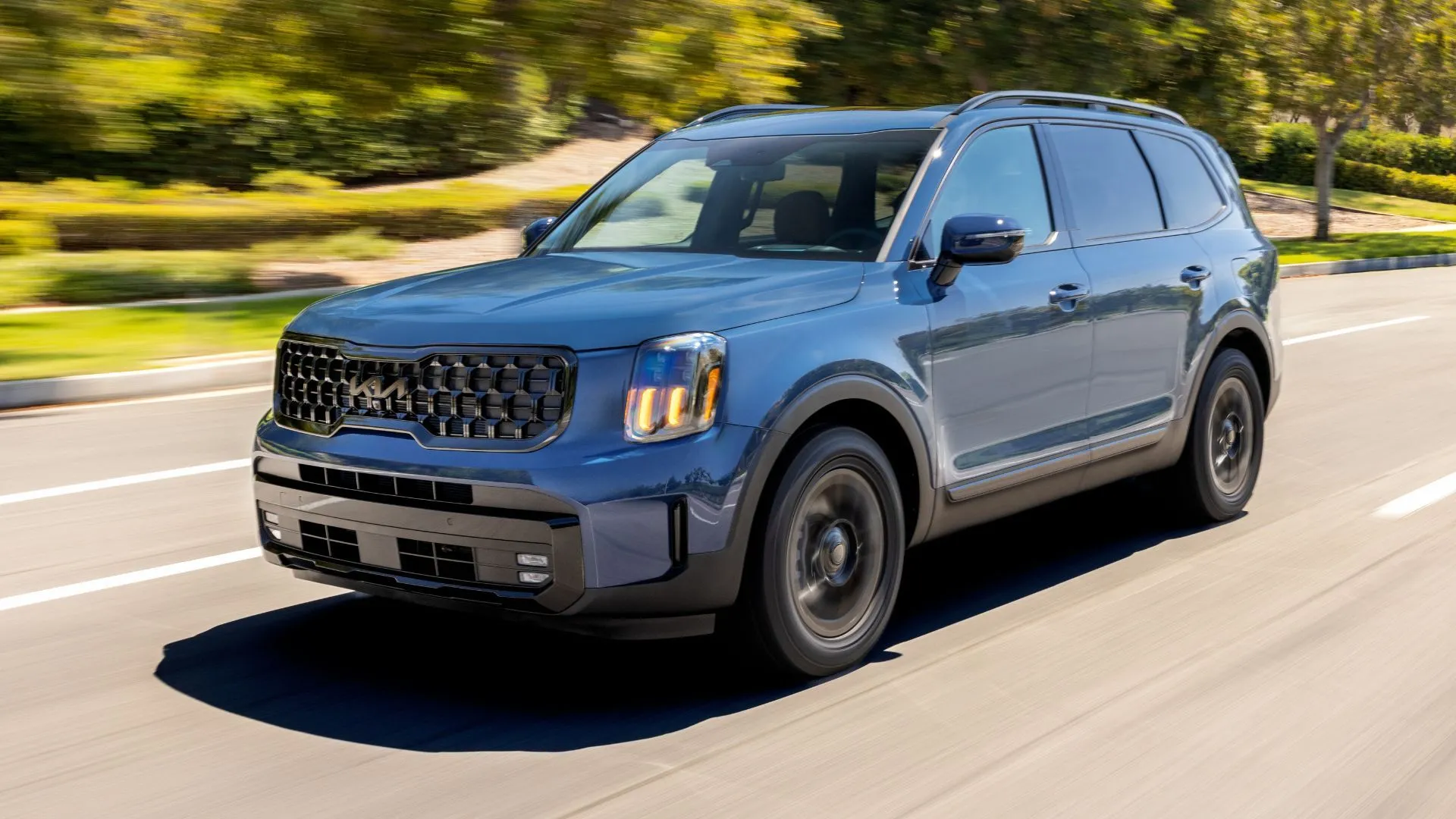Kia Telluride 2025 màu xanh đang di chuyển trên đường cây cối