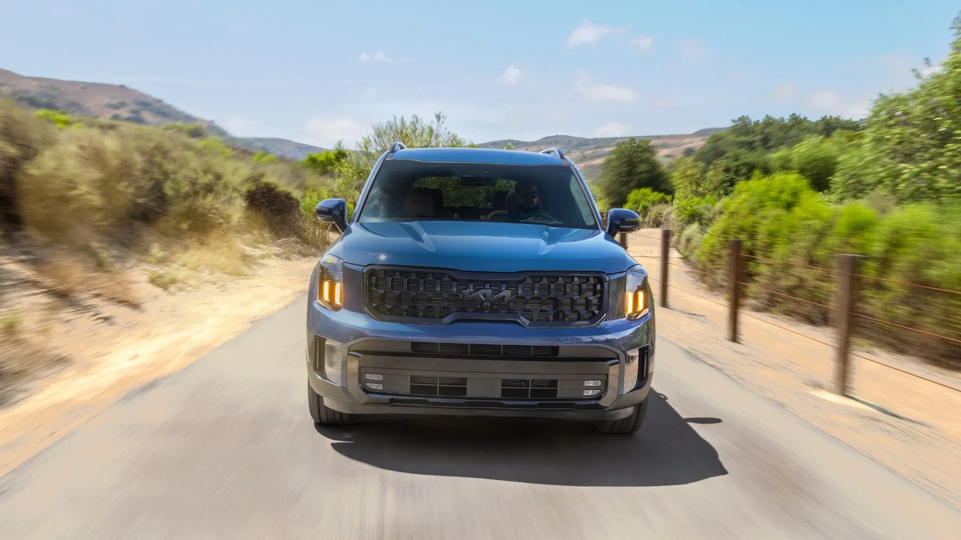 Kia Telluride 2025 màu xanh đang di chuyển trên đường nông thôn