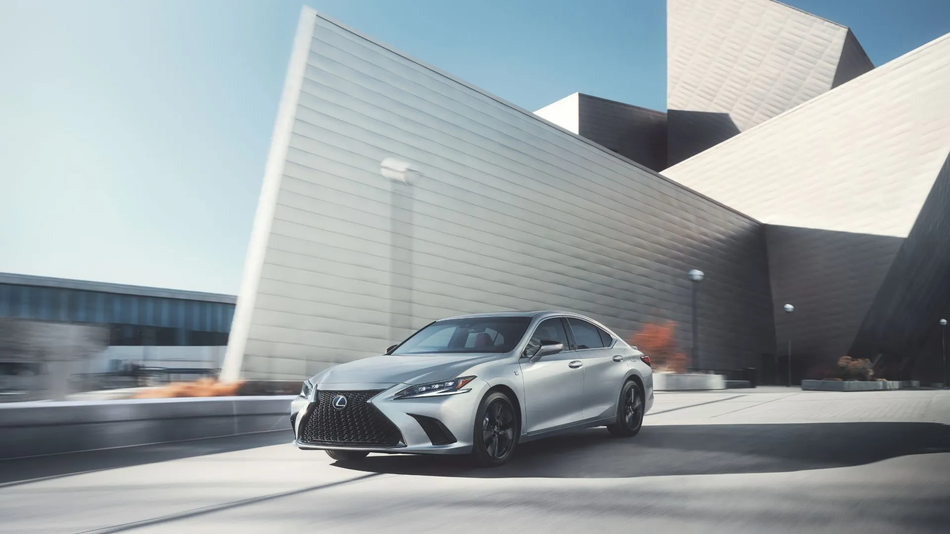 Lexus ES 300h 2023 màu bạc đang chạy trên đường trước một tòa nhà hiện đại
