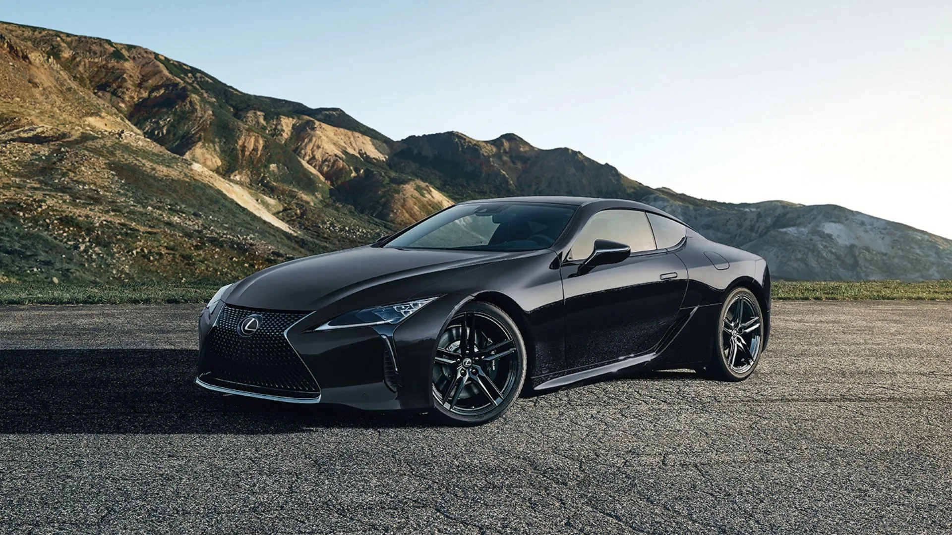 Lexus LC 500 2025 màu đen đỗ trên sỏi với núi phía sau