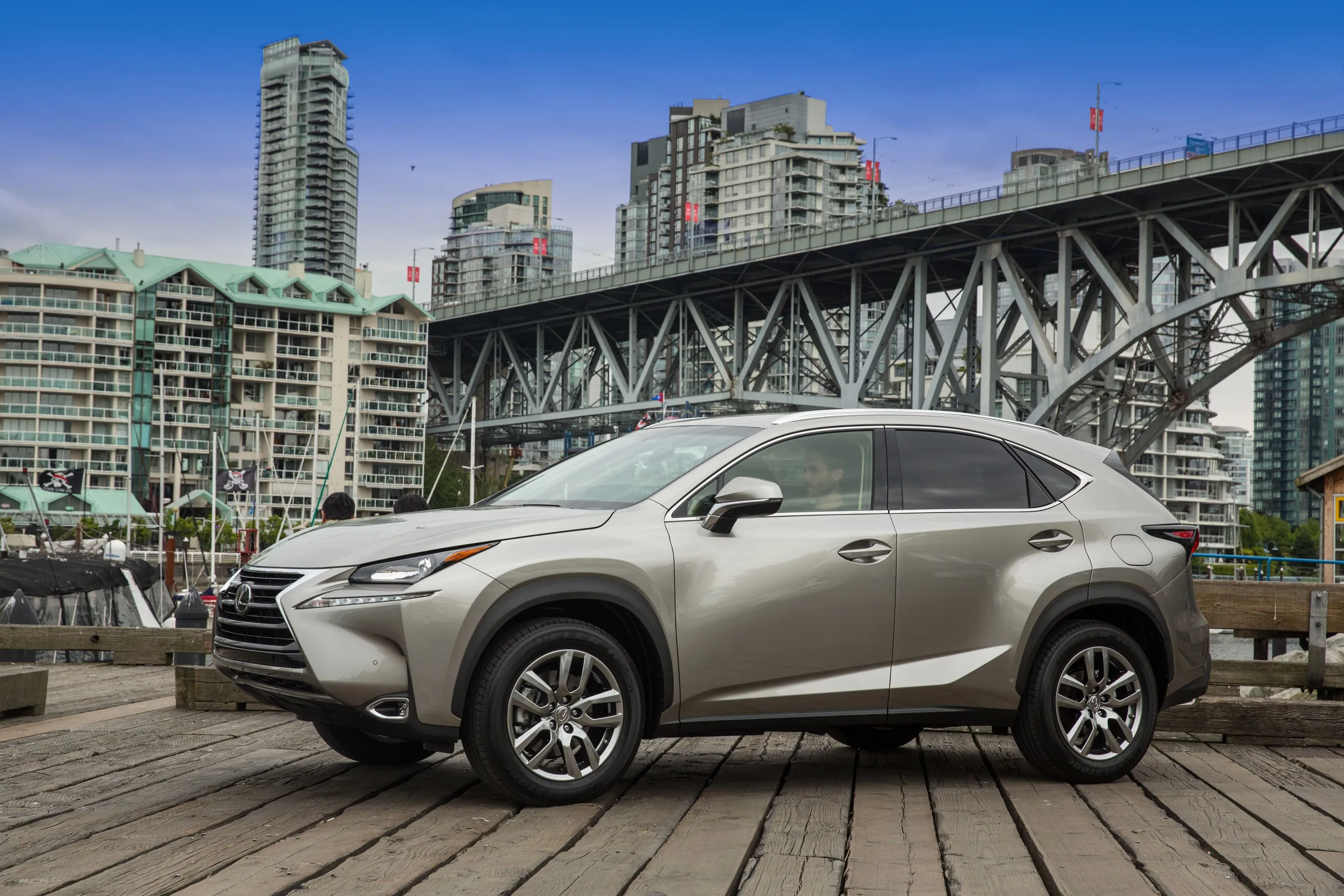 Lexus NX 200t 2017 màu xám đỗ nghiêng trước một cây cầu
