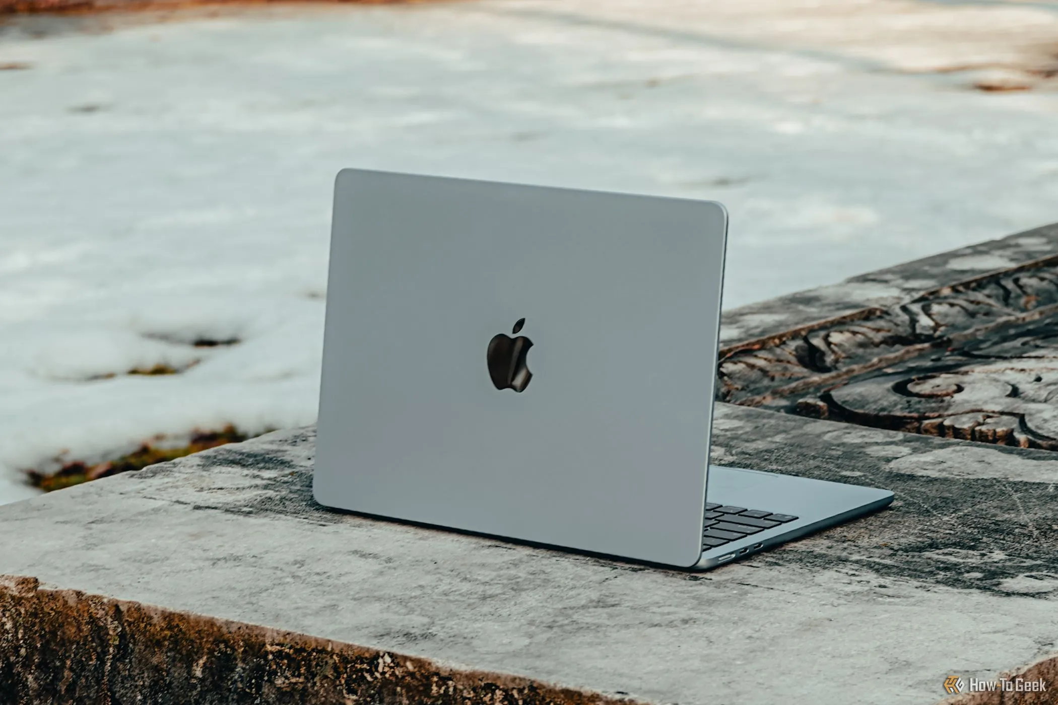 MacBook Air M4 màu xanh da trời đặt trên ghế đá, thể hiện thiết kế mỏng nhẹ nhưng khó sửa chữa