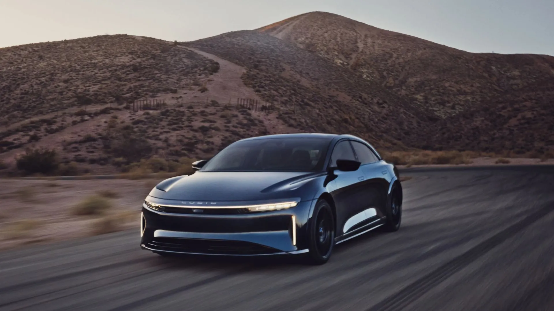Mẫu sedan điện hạng sang Lucid Air màu xanh trên con đường nông thôn, thể hiện thiết kế thanh lịch và tầm hoạt động ấn tượng.