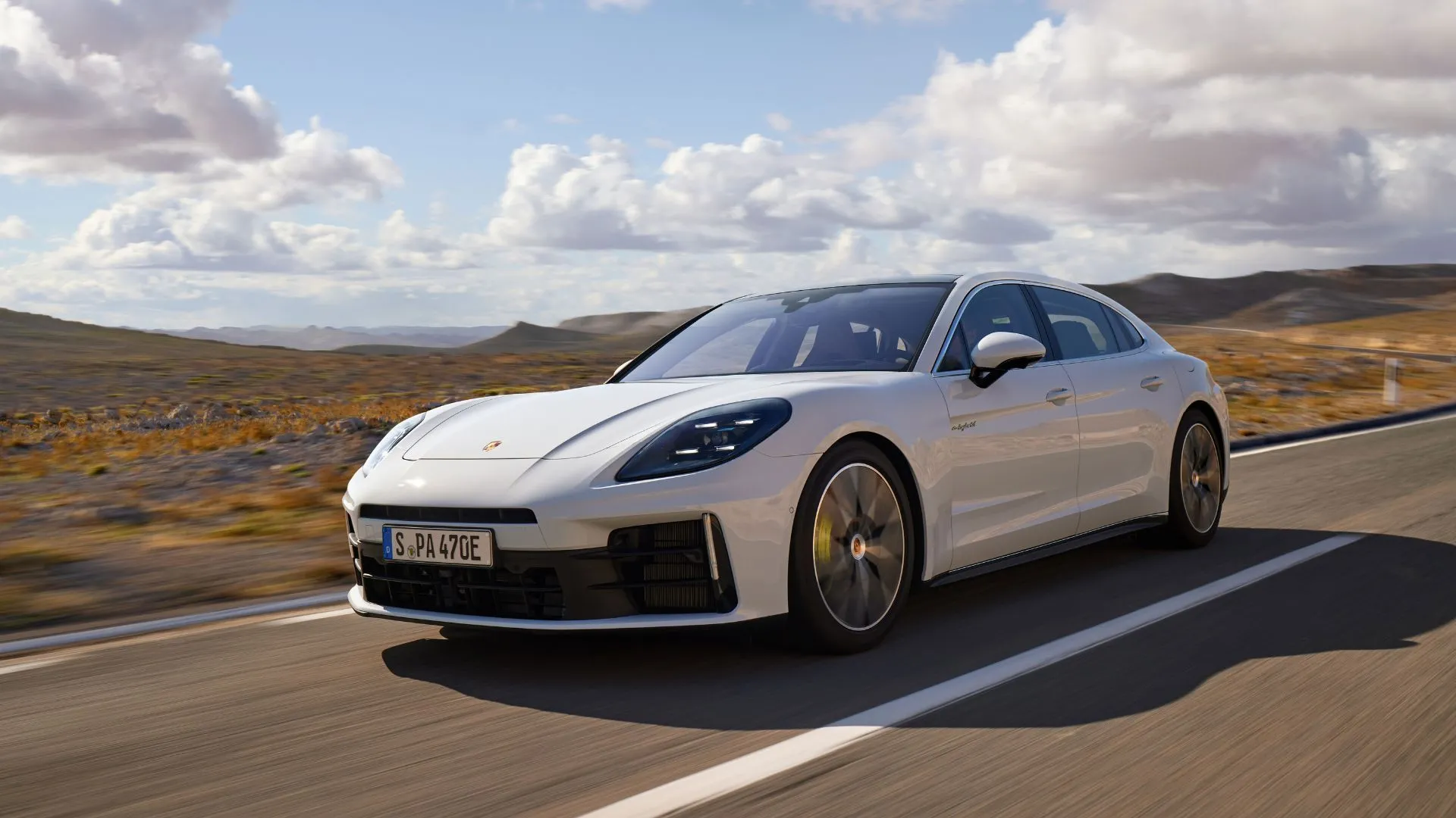 Mẫu xe Porsche Panamera 4 E-Hybrid Executive 2024 màu trắng năng động nhìn từ góc 3/4 phía trước, đang di chuyển trên con đường nông thôn dưới ánh nắng.