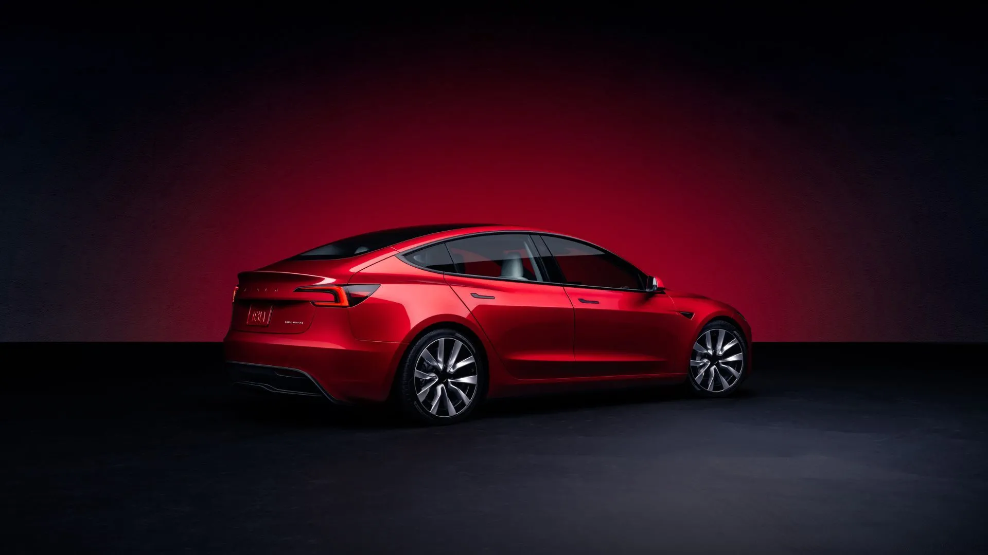 Mẫu xe Tesla Model 3 màu đỏ 2025 chụp từ góc 3/4 phía sau trong studio, nổi bật với thiết kế thể thao