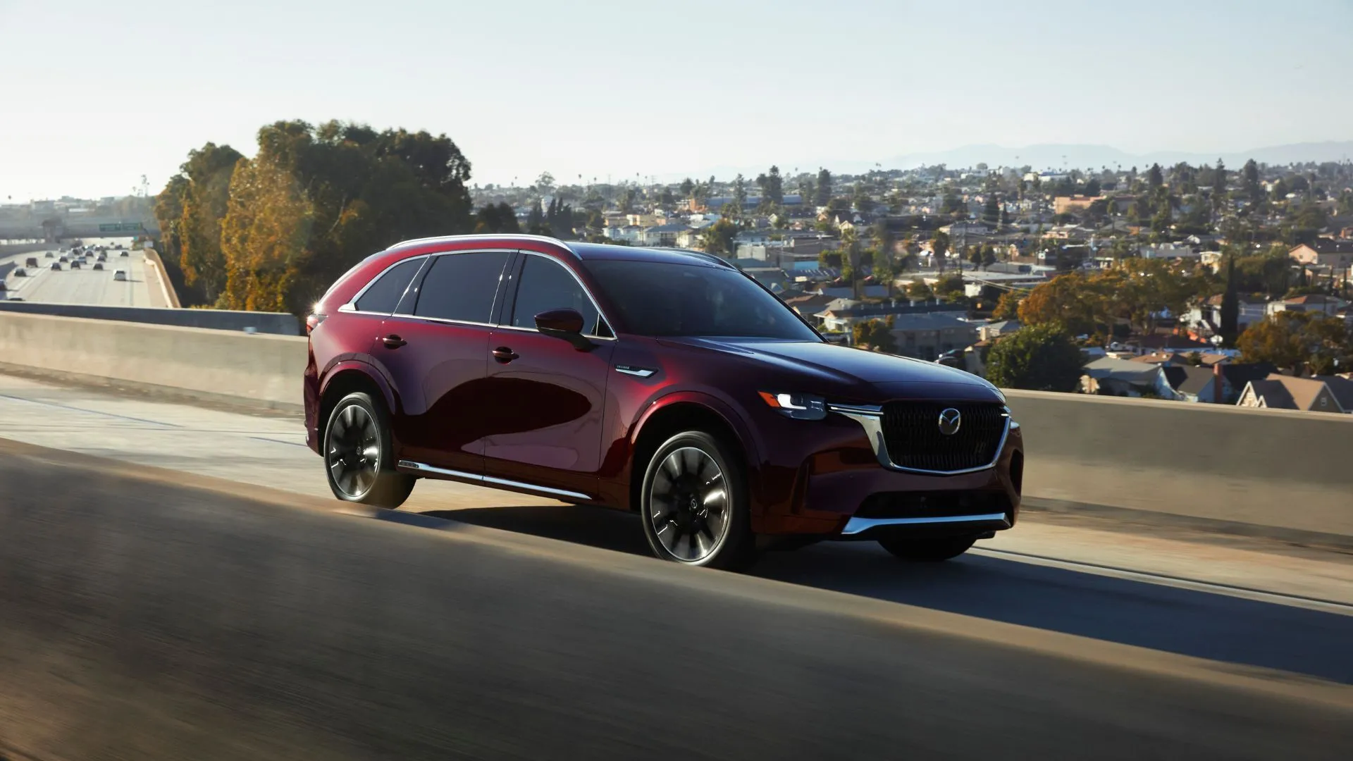 Mazda CX-90 2025 màu đỏ sẫm đang di chuyển trên đường cao tốc, phô diễn phong cách thiết kế sang trọng và không gian 3 hàng ghế.