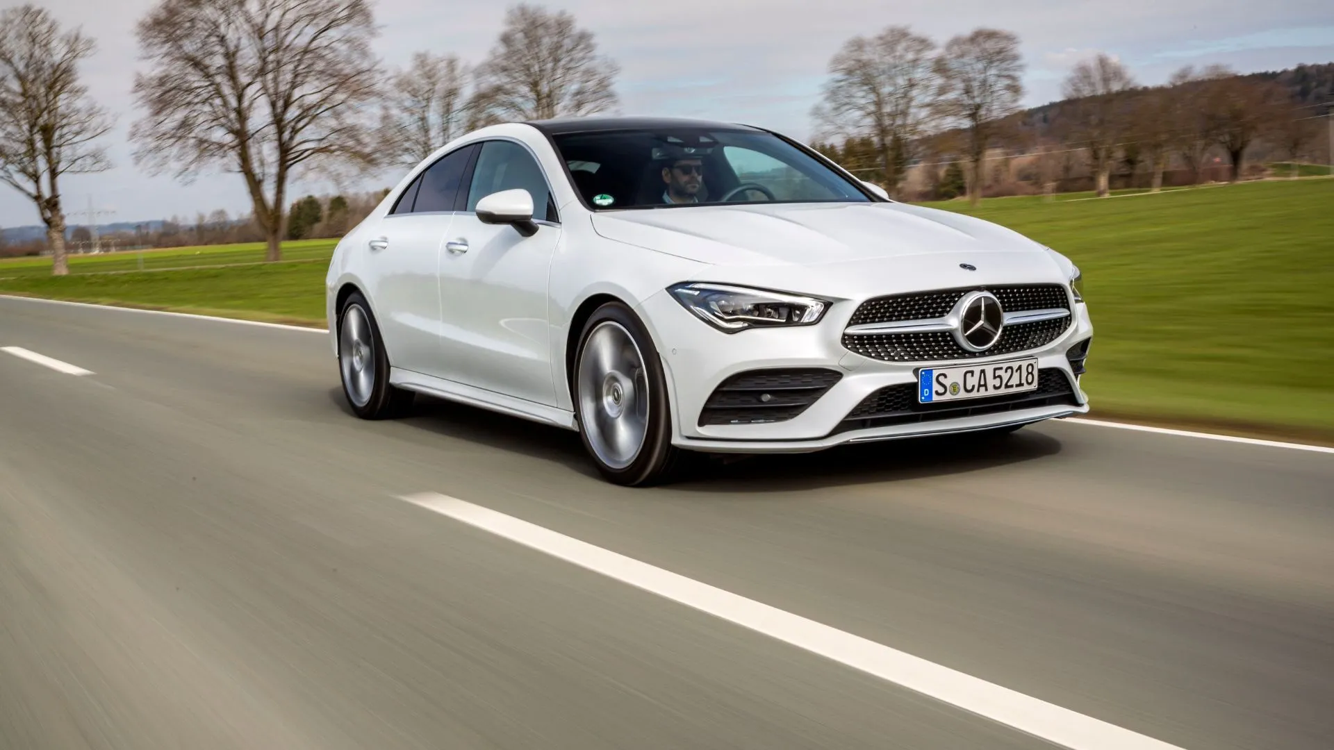 Mercedes-Benz CLA-Class 2025 màu trắng tinh tế di chuyển trên con đường quê, nổi bật với màn hình kép 10.25 inch