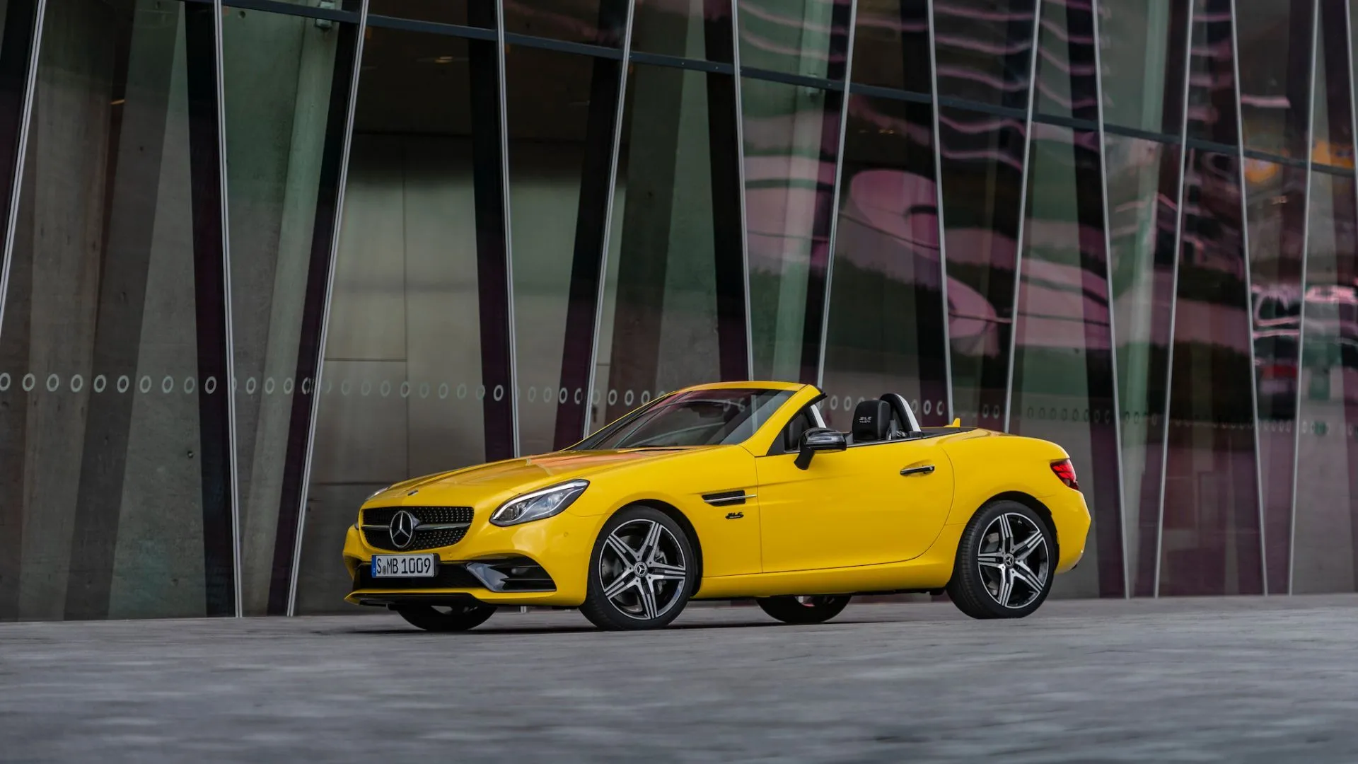 Mercedes-Benz SLC 2020 màu vàng với mui xếp, đỗ trước tòa nhà hiện đại