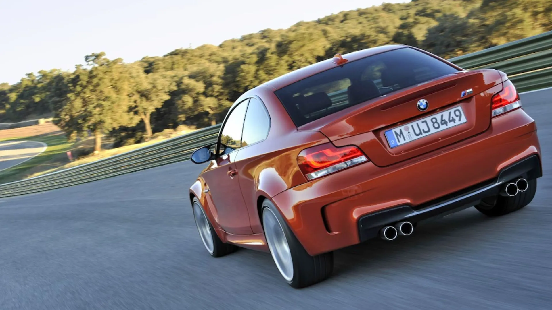 Một chiếc BMW 1M Coupe màu cam đang di chuyển tốc độ cao trên đường đua, biểu tượng của tinh thần M.