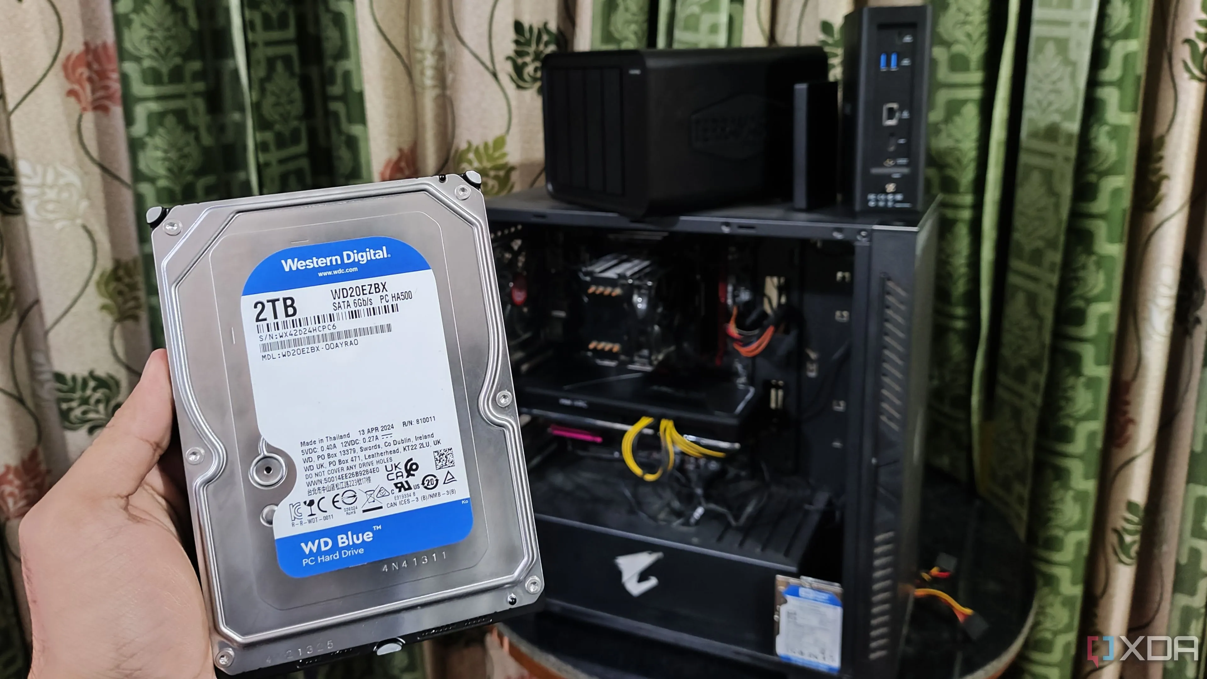 Người dùng đang cầm ổ cứng trước máy tính và hệ thống NAS TerraMaster, minh họa giải pháp sao lưu tại nhà