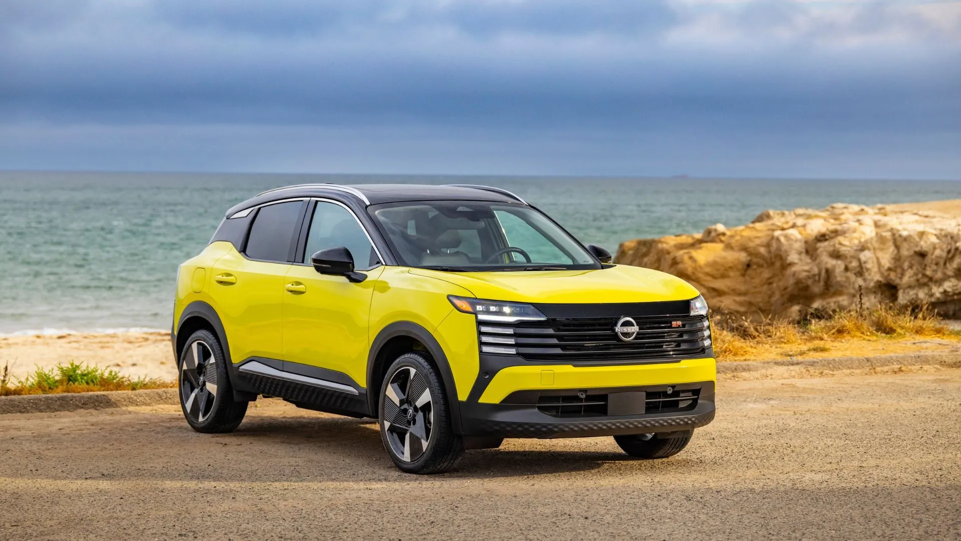 Nissan Kicks 2025 màu vàng đỗ trước biển xanh mát mắt.