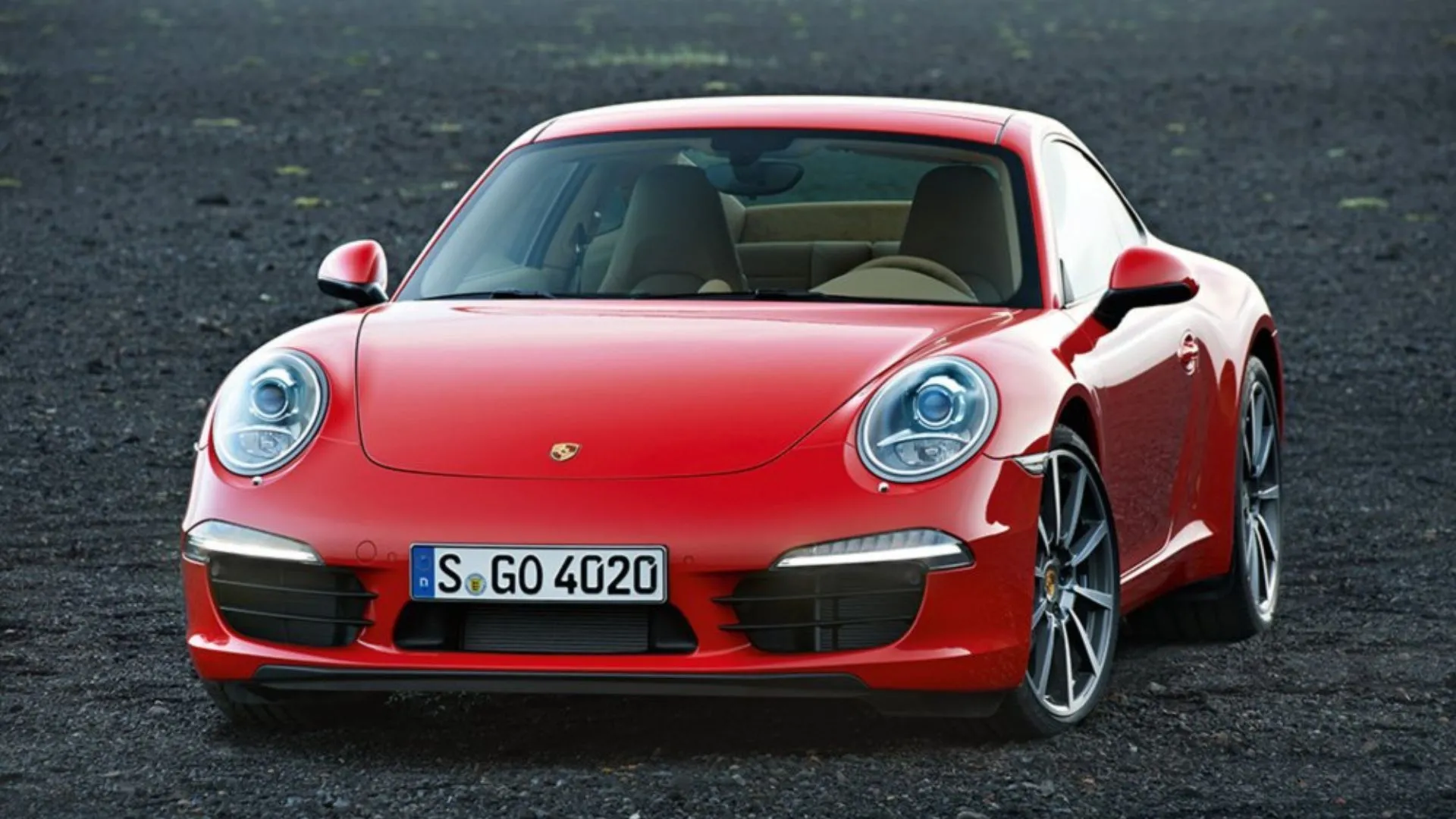 Phần đầu xe Porsche 911 Carrera 991 đời 2012 màu đỏ đậu trên nền sỏi, toát lên vẻ cổ điển và mạnh mẽ.