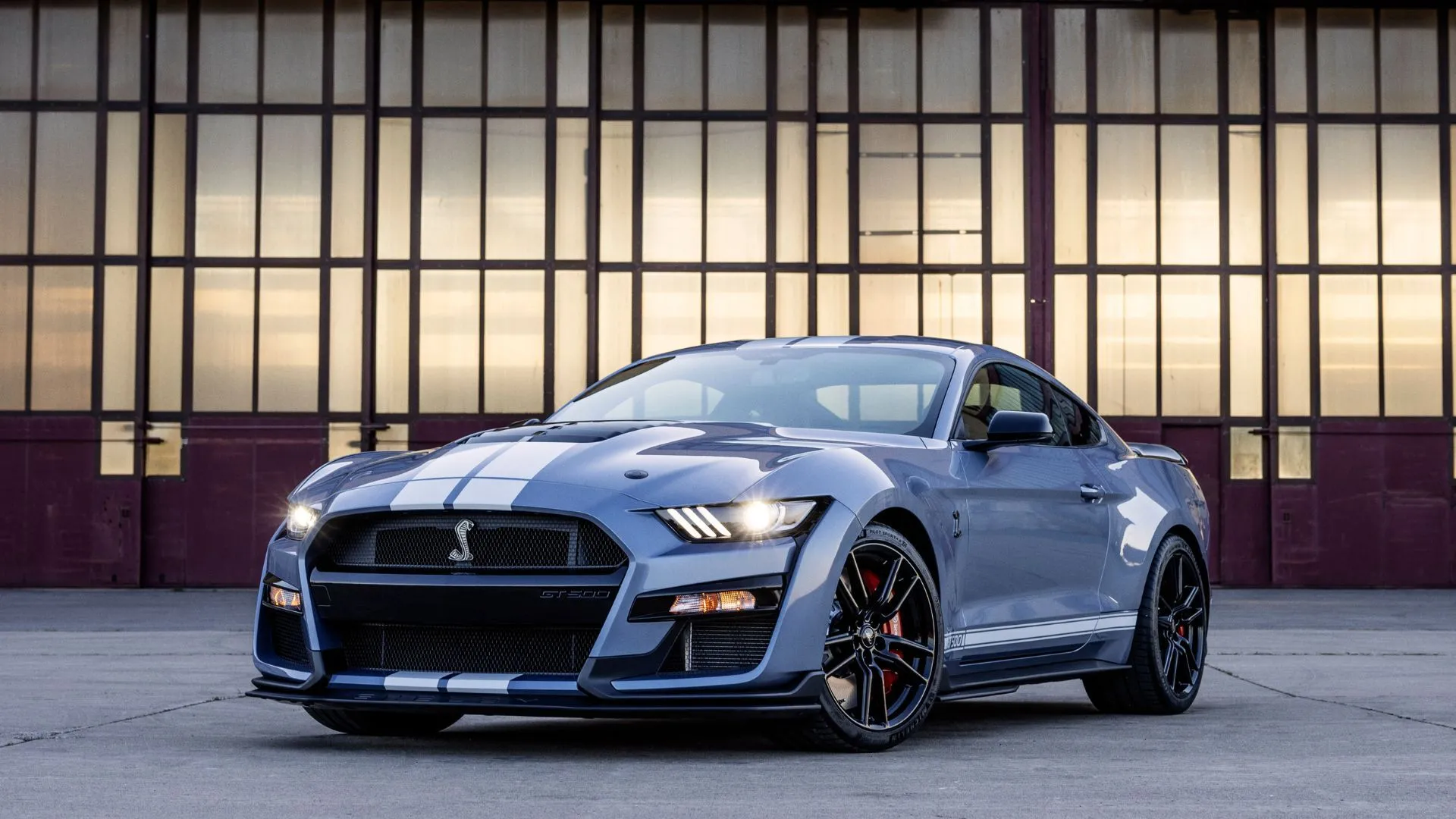 Phiên bản Ford Mustang Shelby GT500 Heritage Edition màu xám đời 2022 đậu nghiêng trước nhà kho, thể hiện sức mạnh cơ bắp Mỹ.