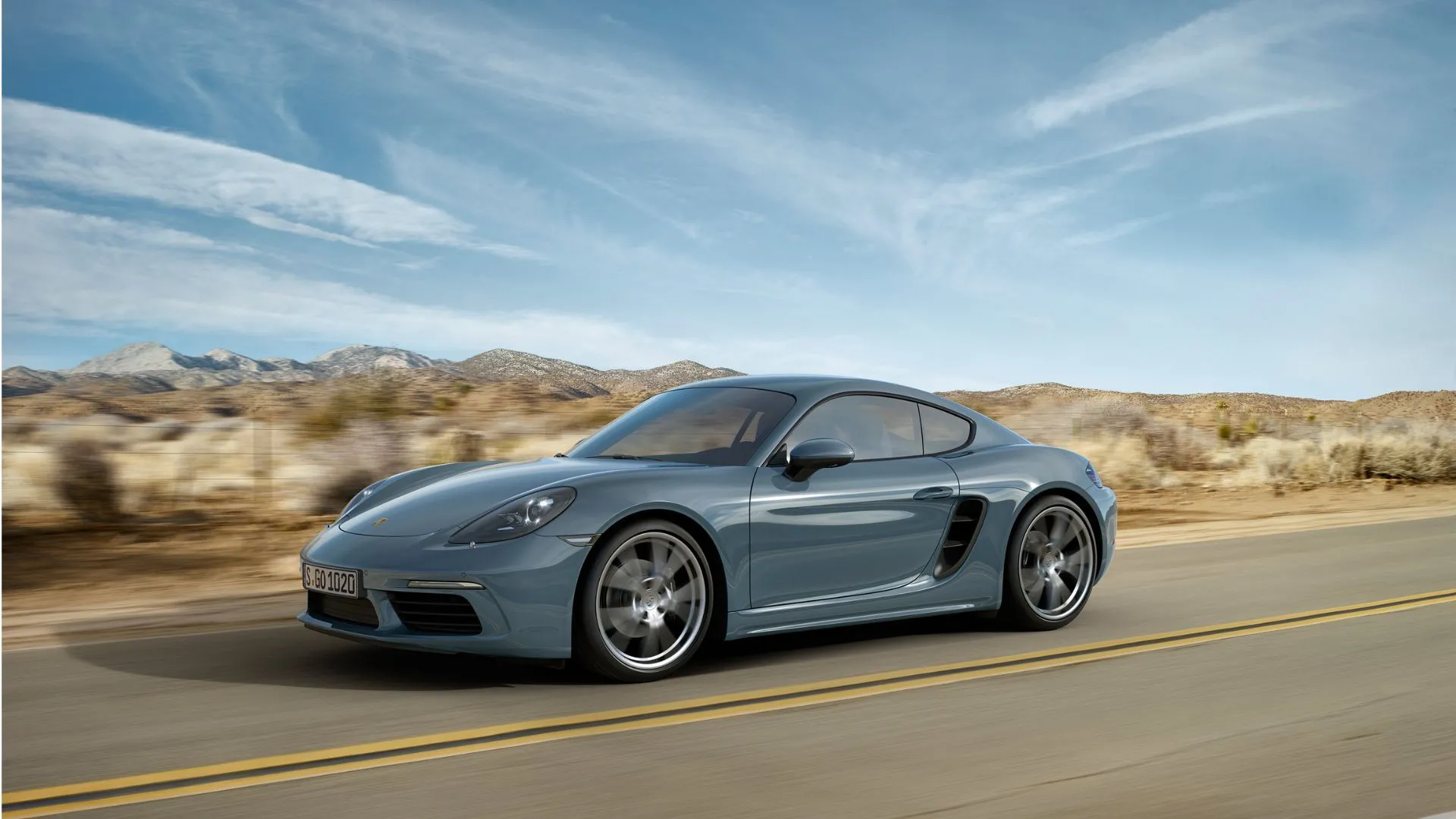 Porsche Cayman 718 màu xám đời 2016 đang chạy trên đường sa mạc, biểu tượng xử lý lái xuất sắc và cân bằng động cơ đặt giữa.