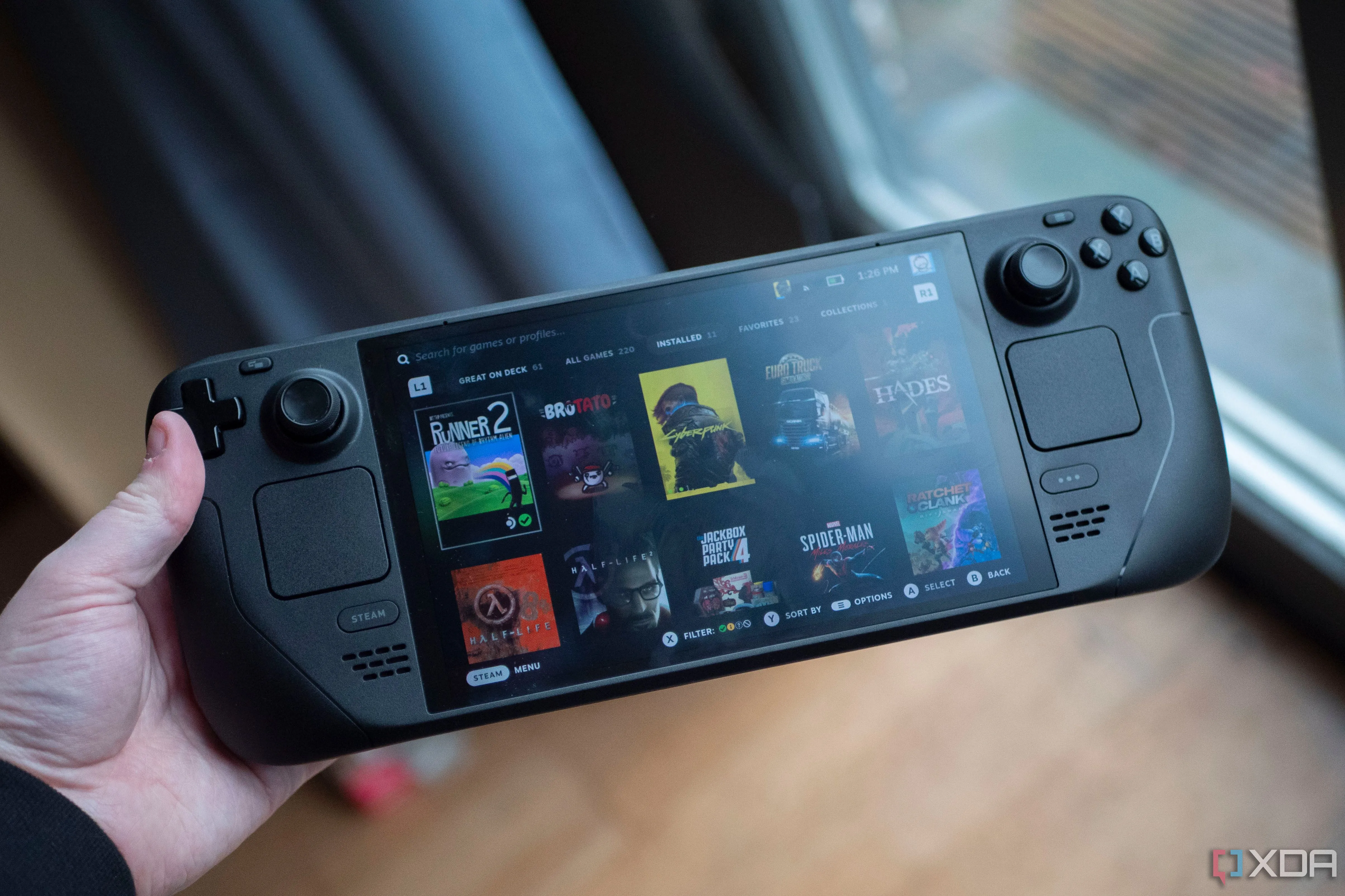 Steam Deck OLED cầm tay với màn hình sáng và các nút điều khiển joystick, thể hiện thiết bị chơi game di động.