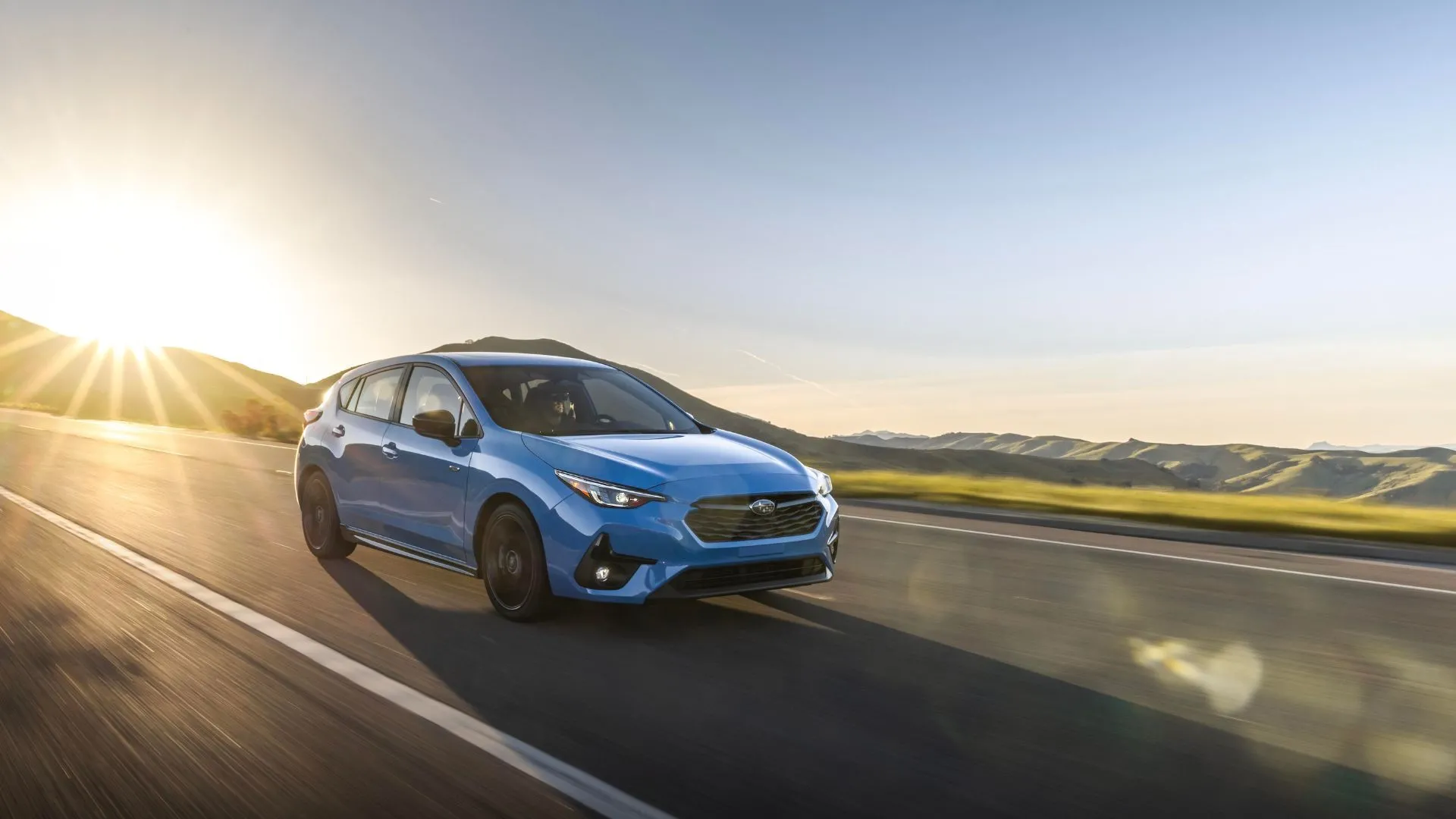 Subaru Impreza 2024 màu xanh lam đang di chuyển trên con đường làng với phong cảnh thiên nhiên