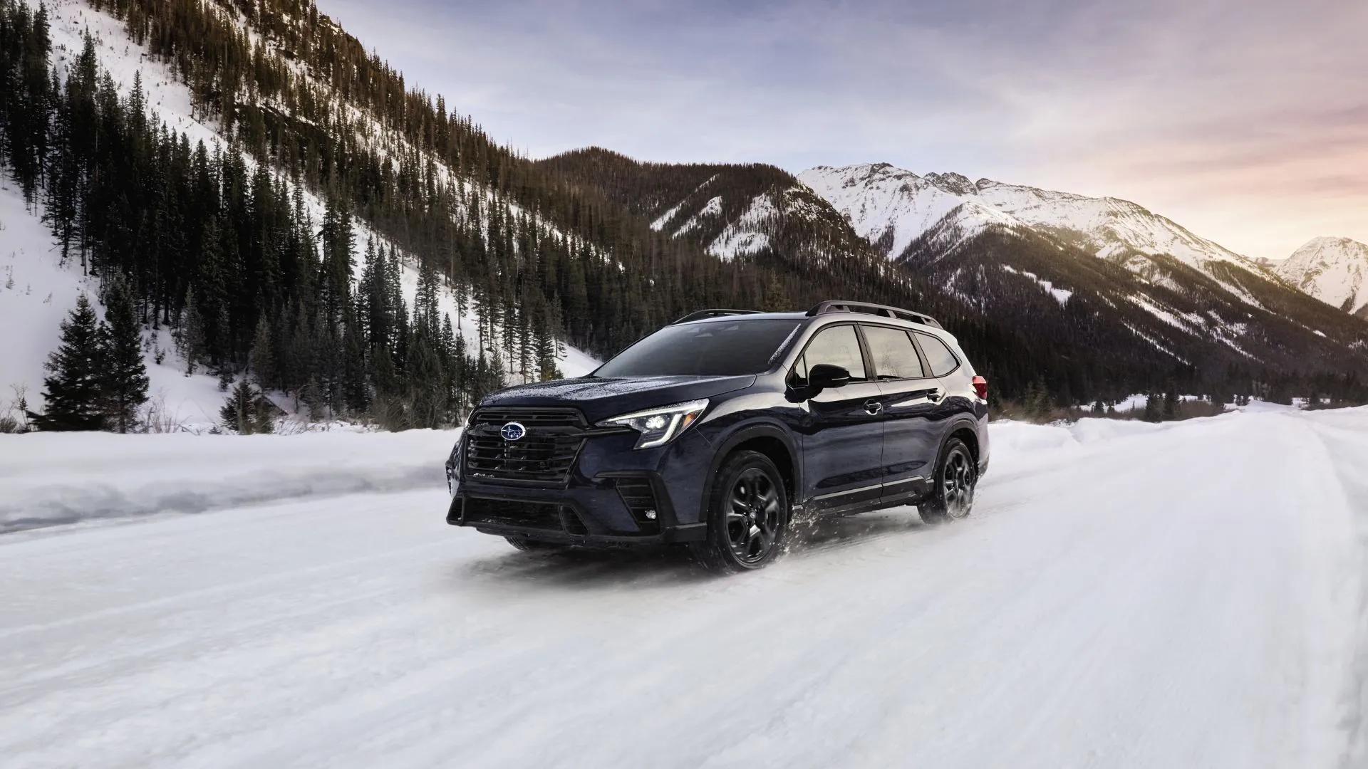 SUV Subaru Ascent 2025 màu xanh đậm chạy trên đường tuyết, phía sau là núi, minh họa sự thực dụng và bền bỉ của Subaru