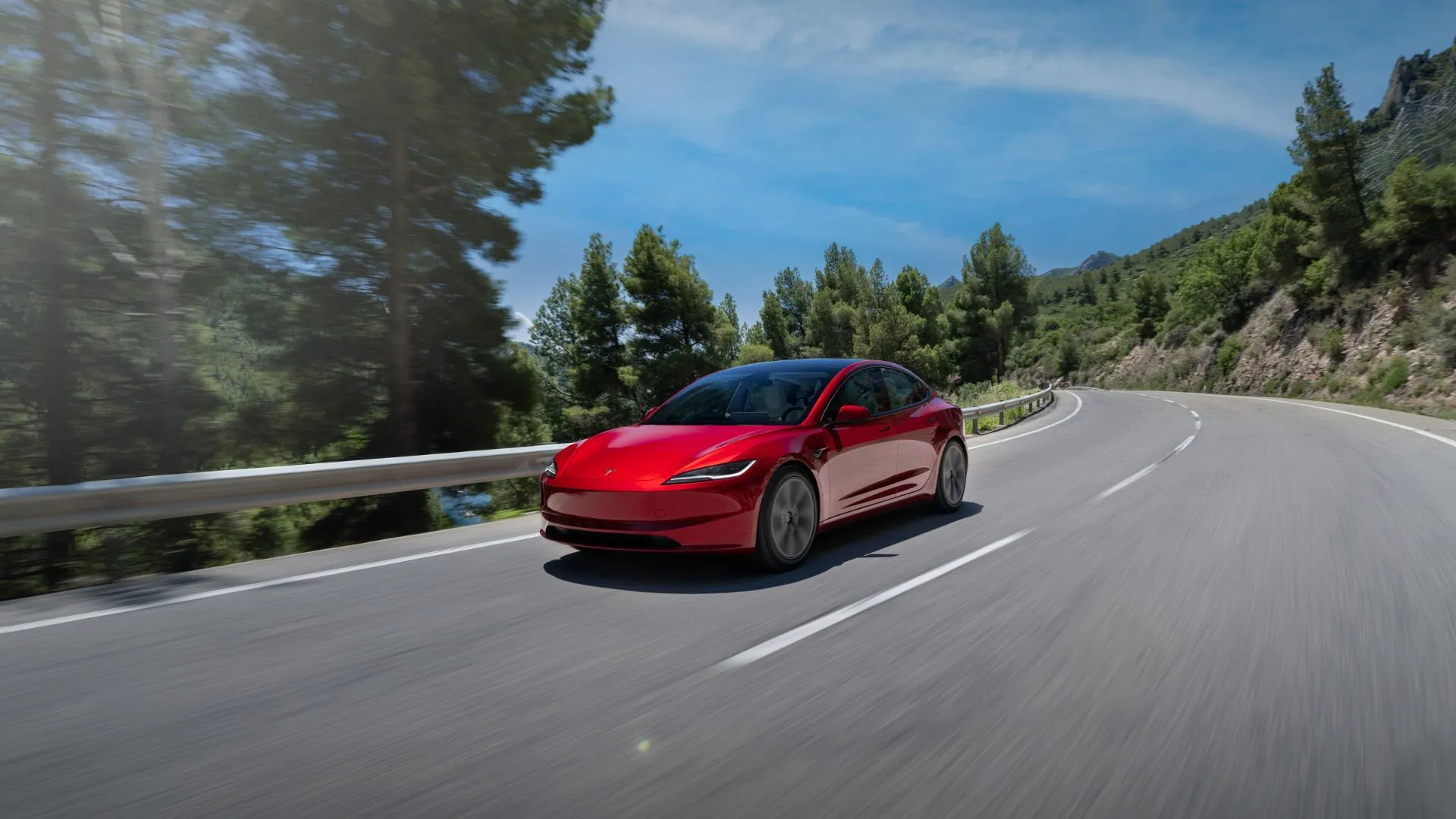 Tesla Model 3 2024 màu đỏ đang chạy trên một con đường nông thôn quanh co.