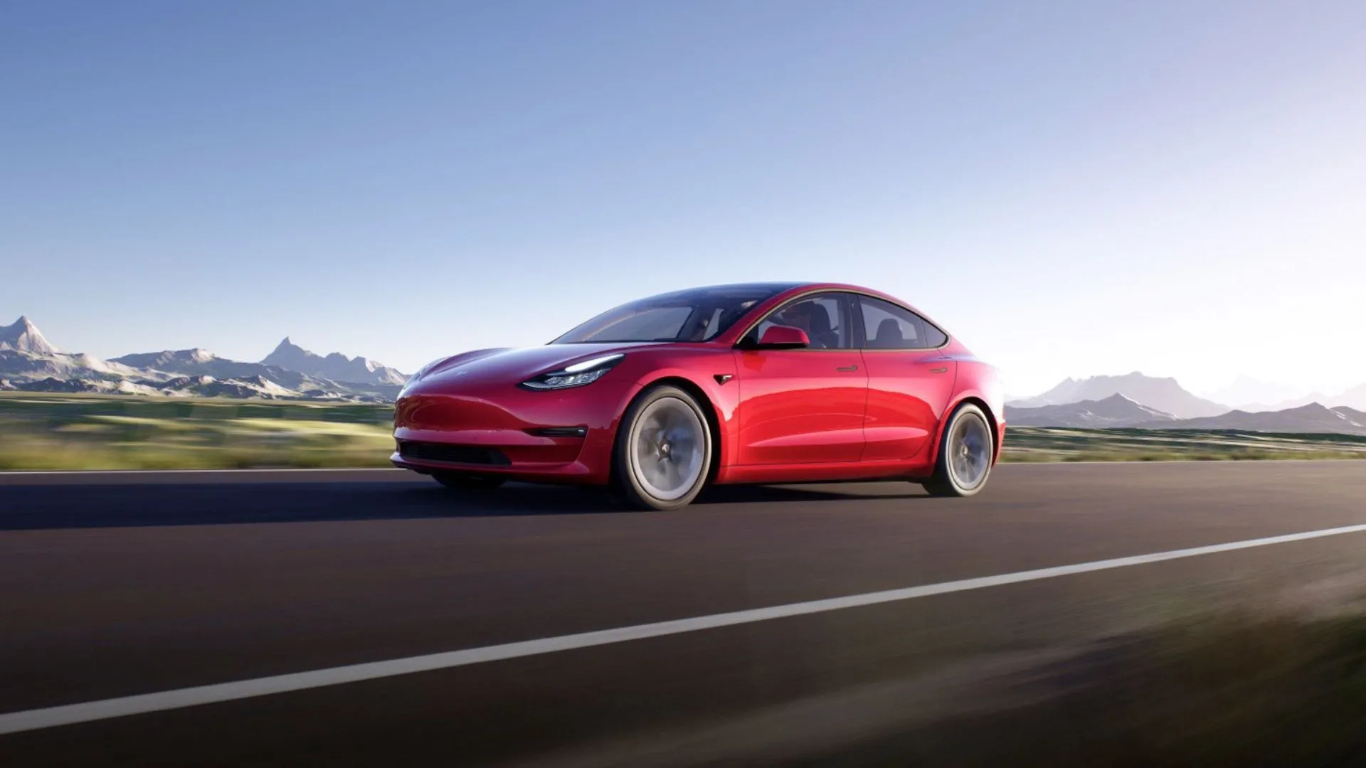 Tesla Model 3 màu đỏ trên con đường nông thôn với núi phủ tuyết phía sau
