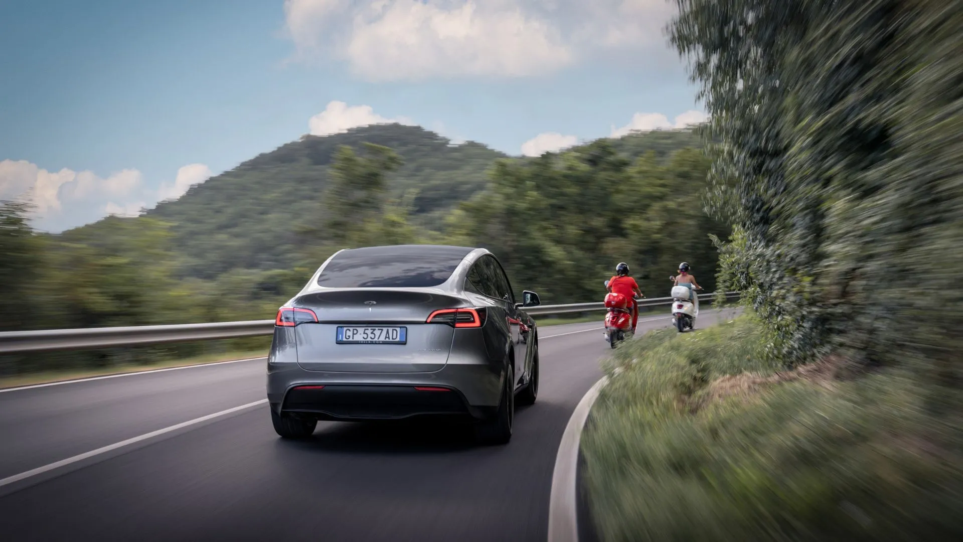 Tesla Model Y màu bạc di chuyển trên con đường nông thôn quanh co, biểu tượng cho tuổi thọ và khả năng vận hành bền bỉ của pin xe điện.