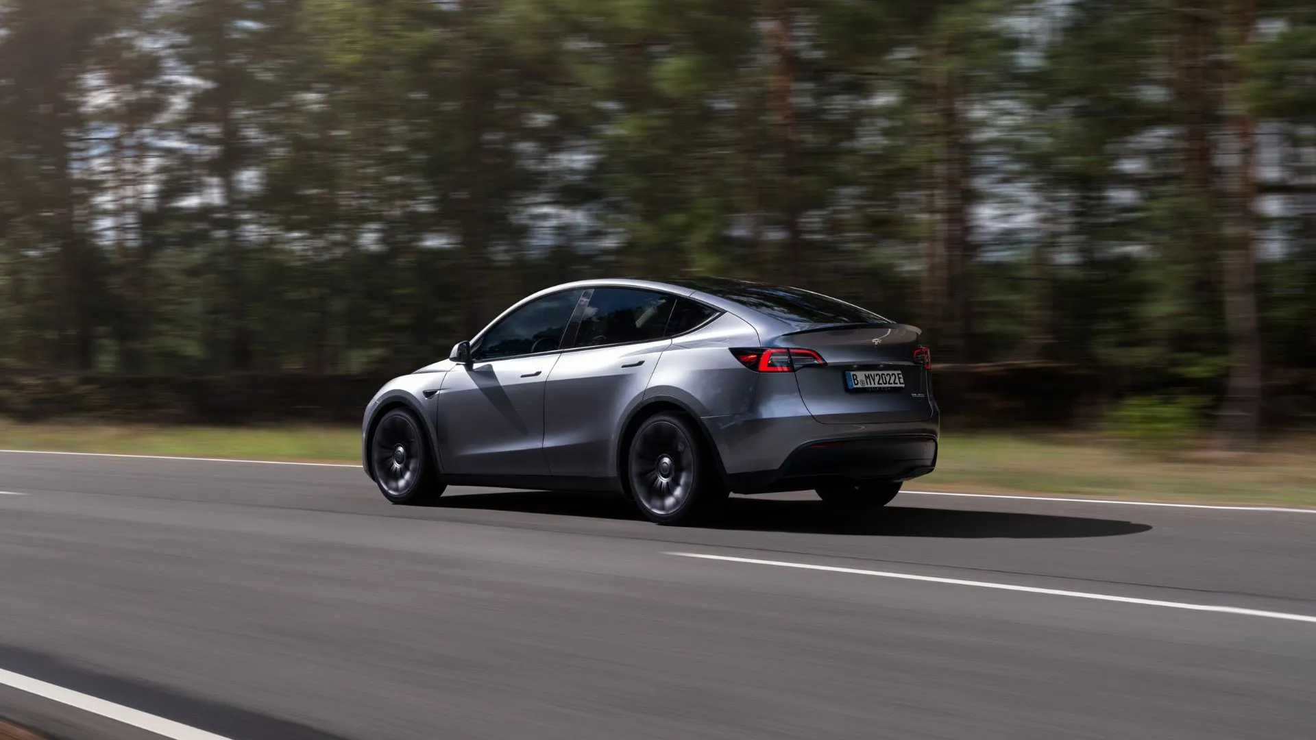 Tesla Model Y màu bạc lái trên đường rừng, tượng trưng cho sự an tâm về chính sách bảo hành pin toàn diện của Tesla.