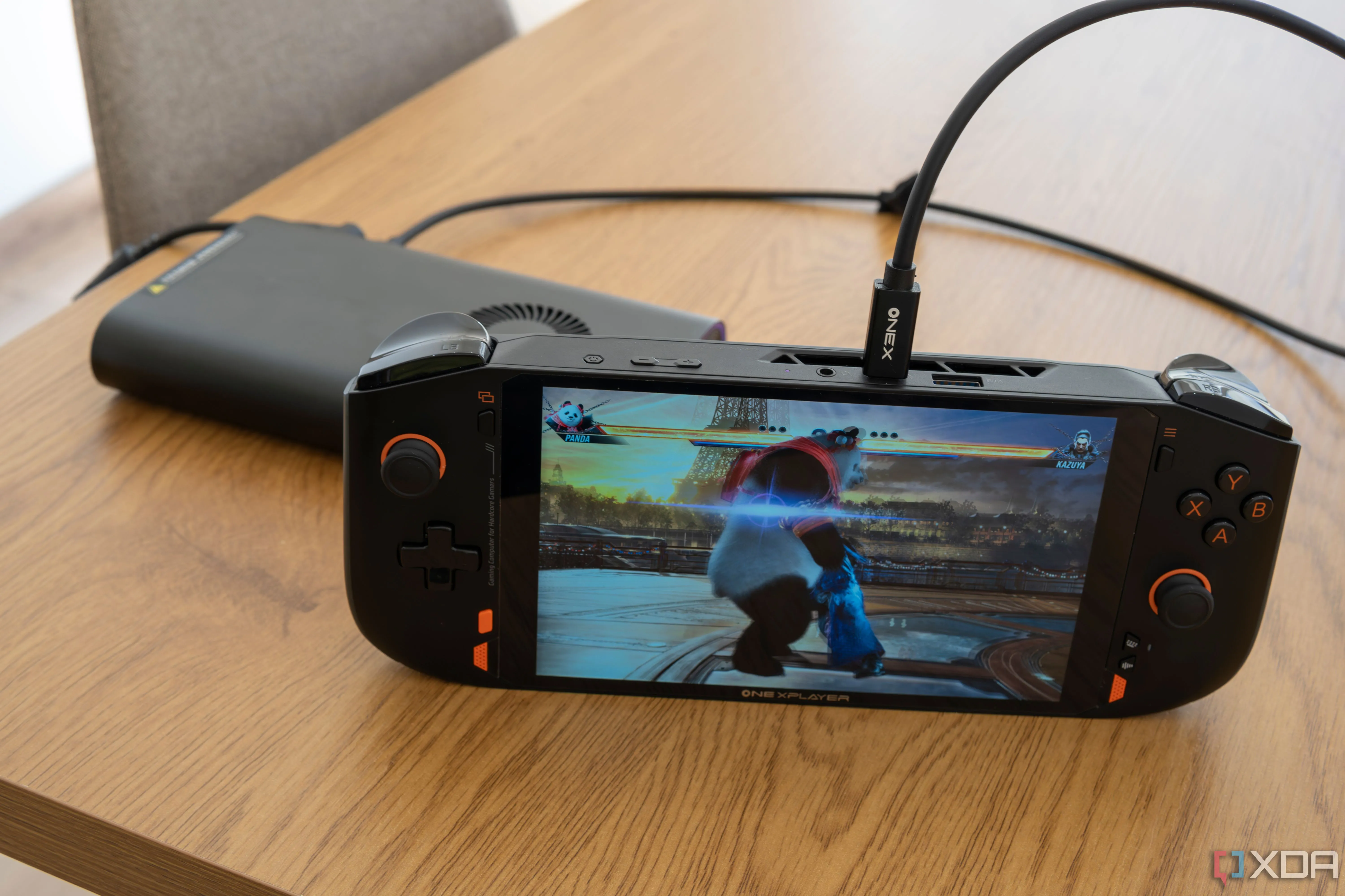 Thiết bị chơi game cầm tay One XPlayer Mini Pro đang chạy game Tekken 8 trước hộp đựng eGPU OneXGPU, minh họa khả năng kết nối và tăng cường hiệu năng