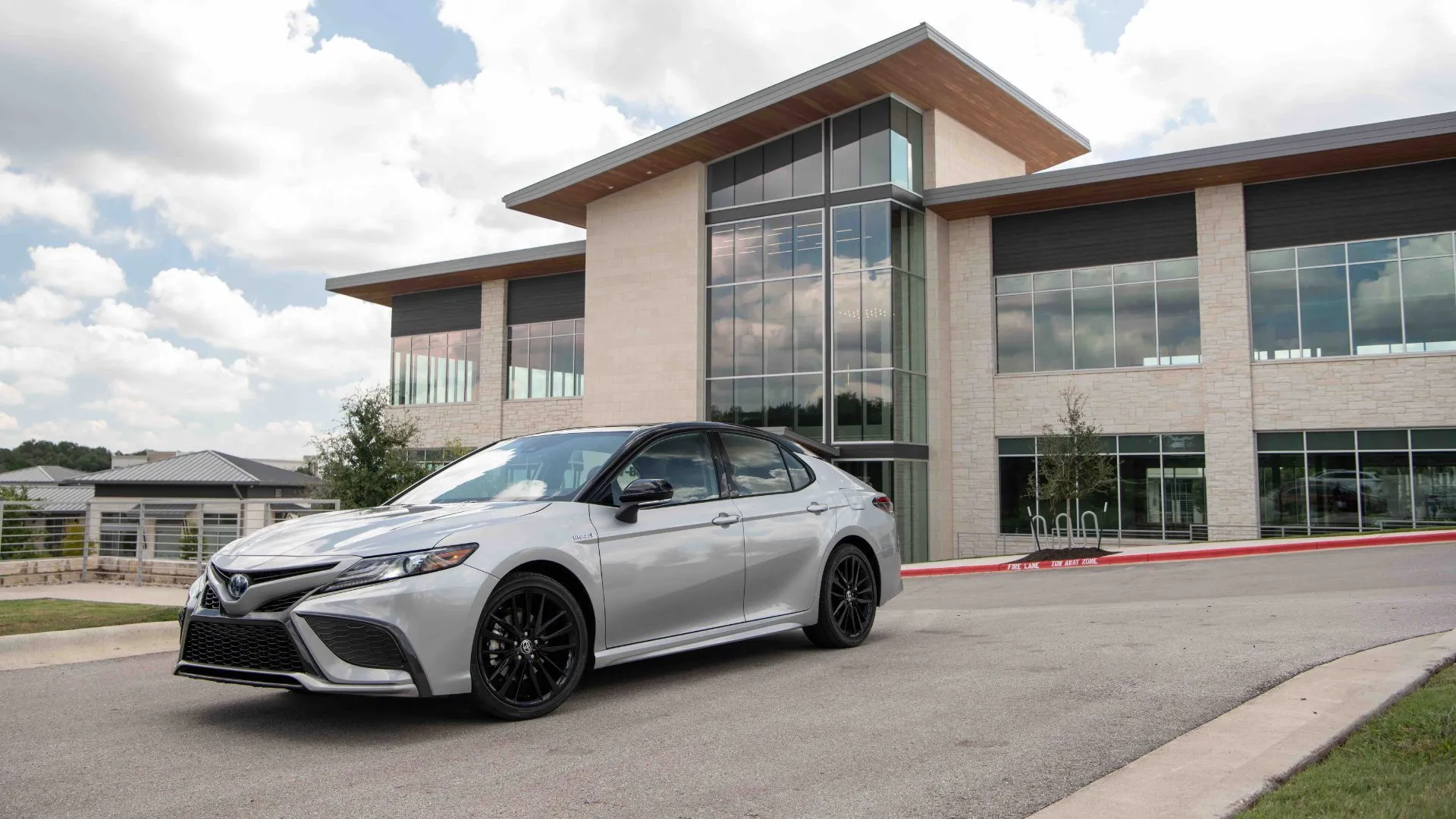 Toyota Camry Hybrid 2022 XSE màu bạc đỗ bên ngoài một tòa nhà hiện đại, thể hiện vẻ sang trọng và phù hợp cho cuộc sống đô thị.