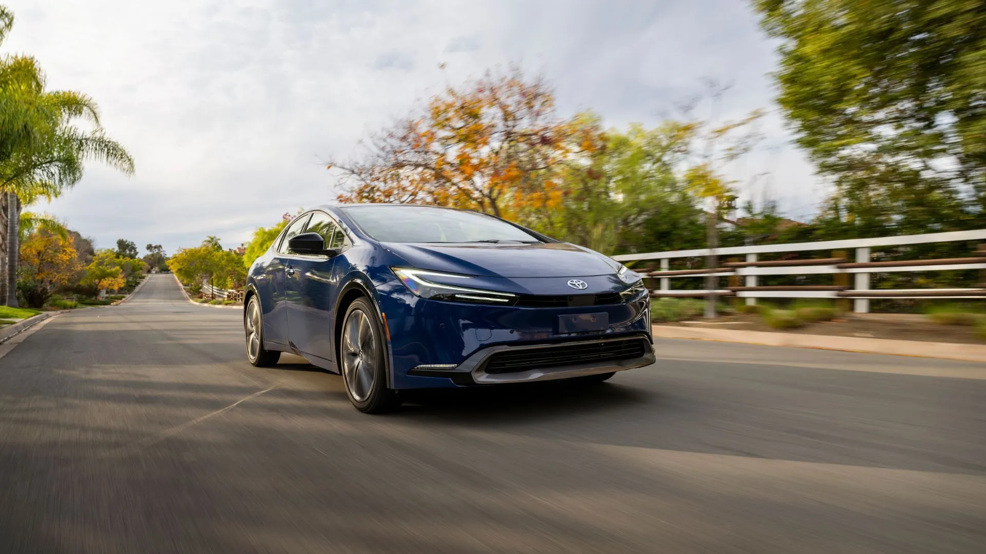 Toyota Prius 2025 màu xanh navy chạy trên đường nông thôn, góc nhìn 3/4 phía trước.