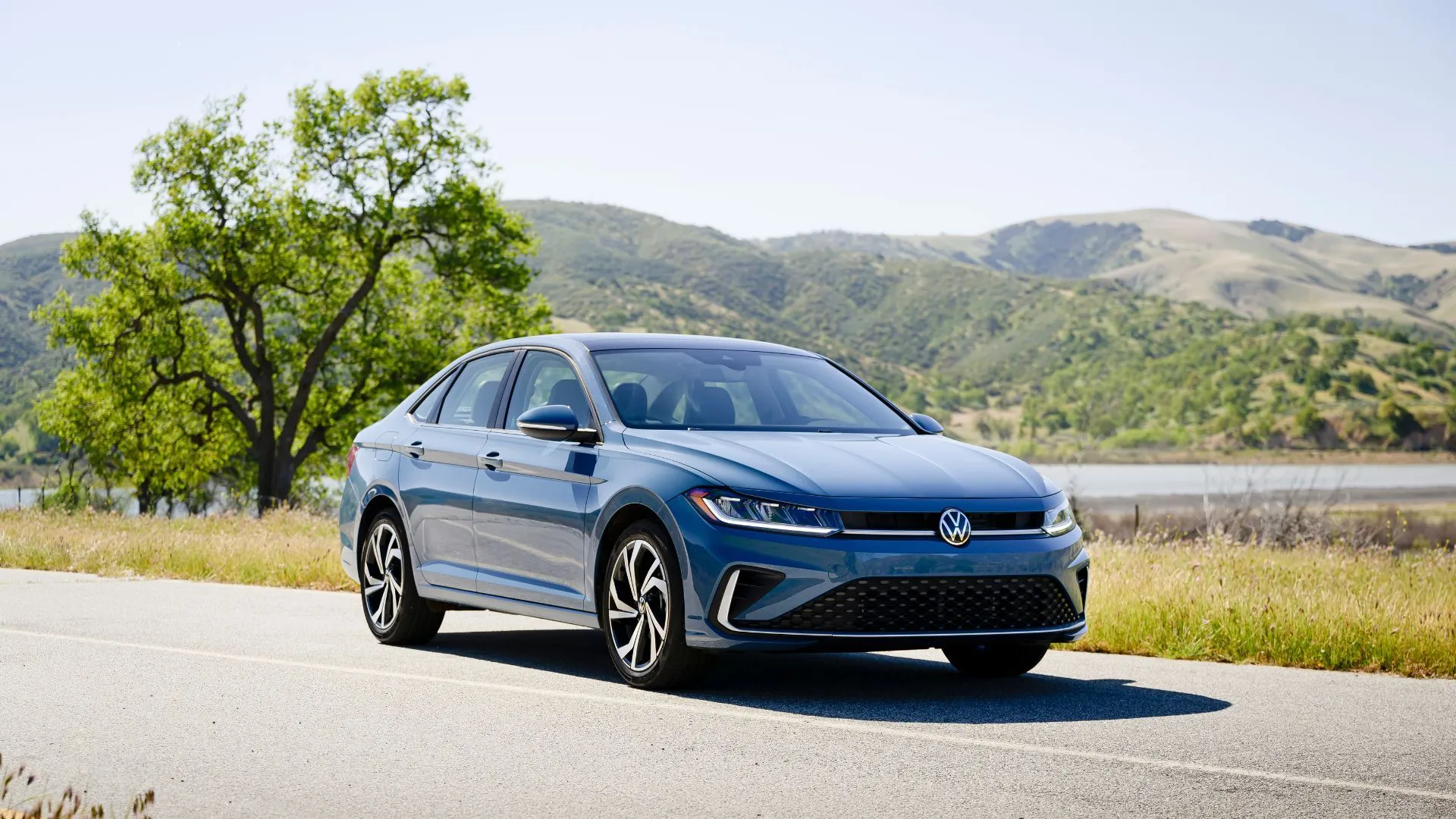 Volkswagen Jetta 2025 màu xanh đỗ trước hàng cây và những ngọn đồi.