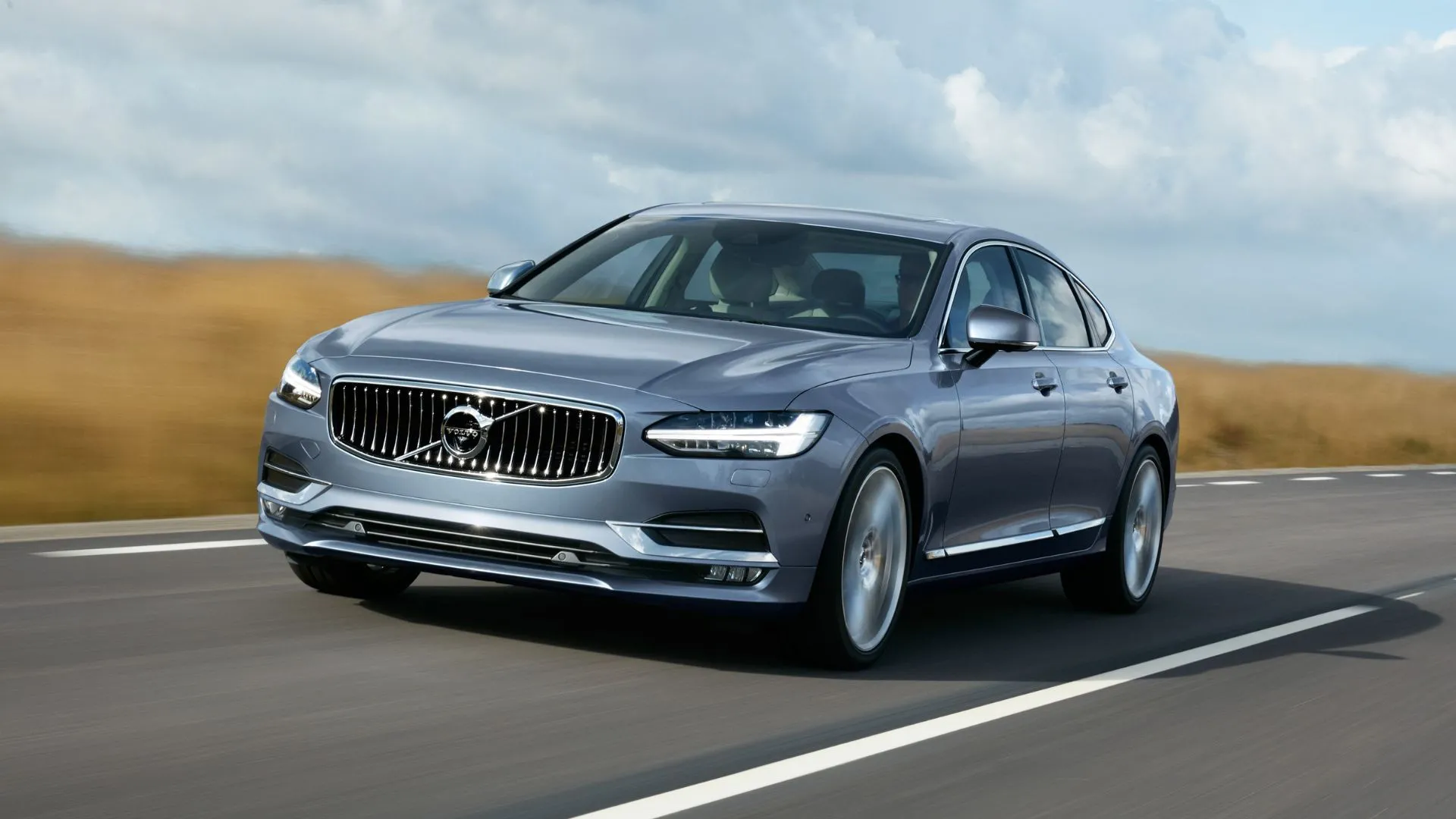 Volvo S90 T6 Inscription Sedan 2019 màu xanh lam di chuyển trên đường quê, nổi bật với thiết kế Scandinavia thanh lịch và động cơ twin-charged mạnh mẽ của dòng xe sang Volvo