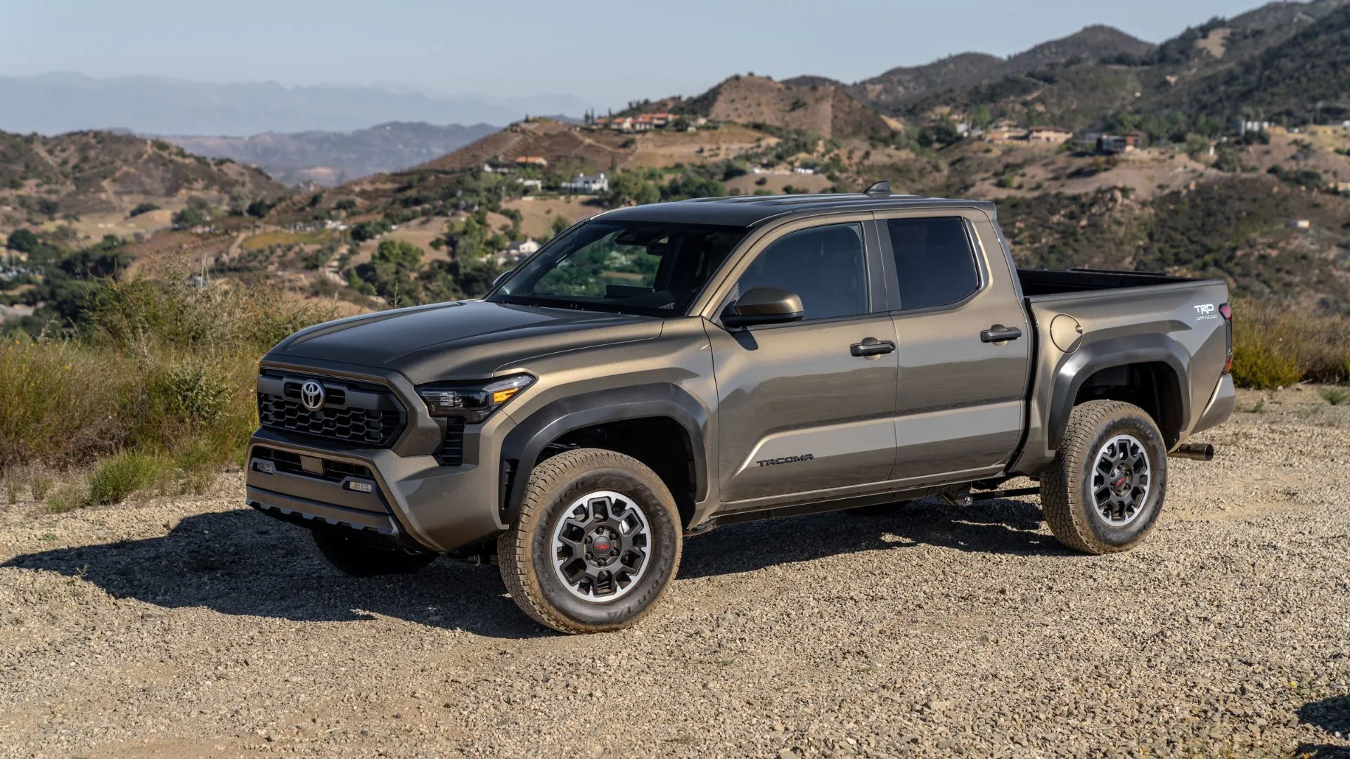 Xe bán tải Toyota Tacoma TRD 2025 màu đồng đỗ trên sỏi, phía sau là núi, phản ánh sự thành công của Toyota tại Mỹ