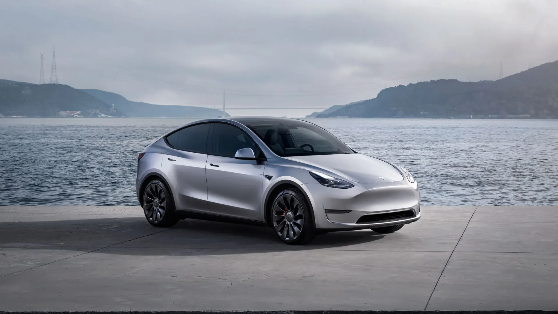 Xe Tesla Model Y màu bạc đỗ bên bờ vịnh với núi non hùng vĩ, minh họa xe điện phổ biến